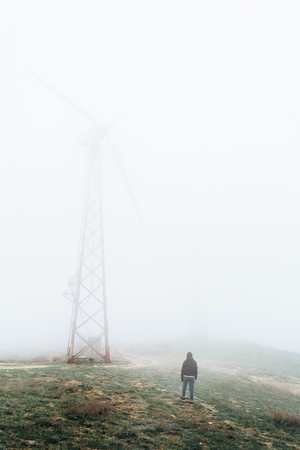 One man looks at huge wind farms, covered with fog, high in the mountains.