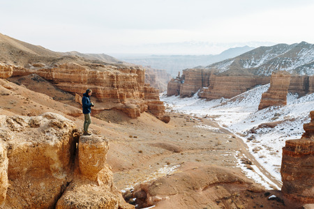 A cheerful traveler with a camera stands on the edge of the cliff in the Charyn canyon in...