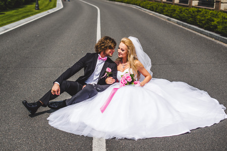 Wedding couple sitting on ground. love symbols on pavement. hearts. people in love. happy bride and groom portraits. man and woman sitting back to back outside on road. newlyweds. wedding dayの写真素材