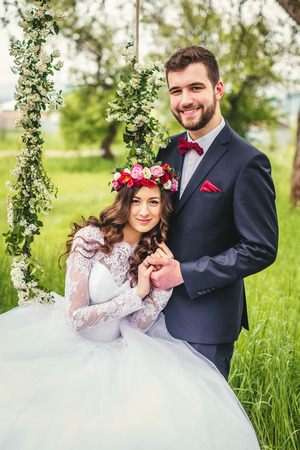 beautiful gorgeous brunette bride and stylish groom on the decorated swing on the treeの写真素材