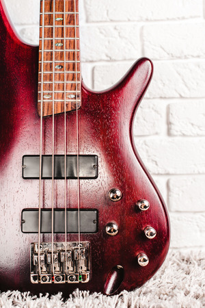 Rosewood bass electric guitar with four strings near the white brick wall closeupの写真素材