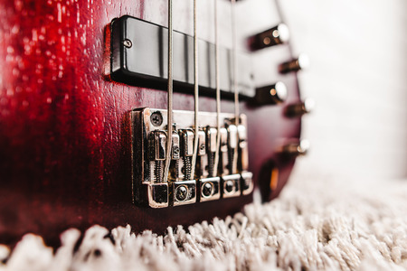 Rosewood bass electric guitar with four strings near the white brick wall closeup