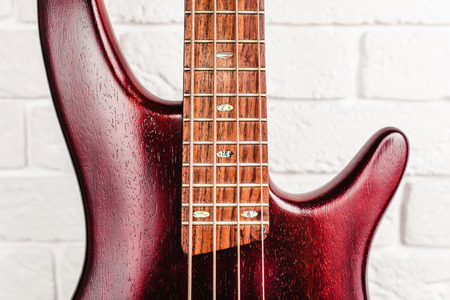 Rosewood bass electric guitar with four strings near the white brick wall closeupの写真素材