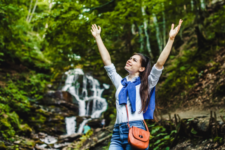 Happy young woman spreading hands enjoying nature with waterfall in background.の写真素材