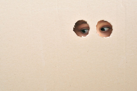 Eyes looking through a hole on coardboard, close upの写真素材