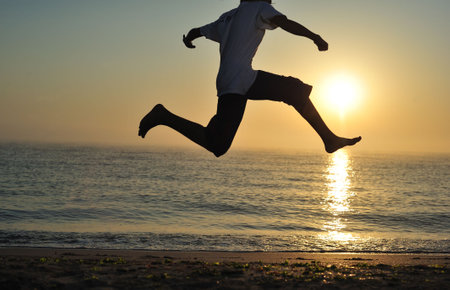 Young boy jumping on beach at sunriseの写真素材