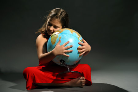 Little girl in red dress embracing Earth globeの写真素材