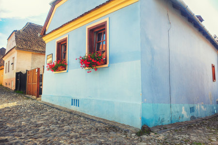 Old house with flowers window on a paved street of the Fortress Sighisoara in Romania, Transylvaniaのeditorial素材