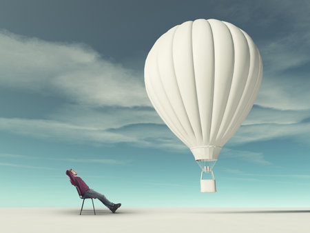 Man sits on  chair and looks at a white hot air balloonの写真素材