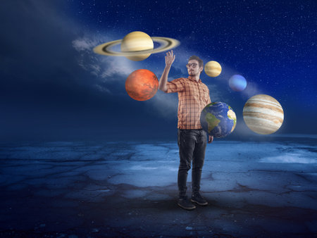 Young man in middle of solar system pointing to a planet into the night.の写真素材
