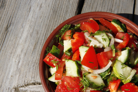 salad of tomatoes, cucumbers, onions, in a dark plate on a wooden table in the sunlight の写真素材