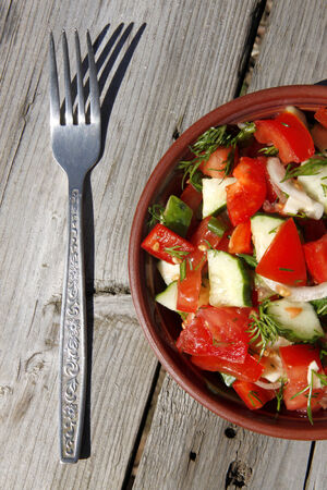 salad of tomatoes, cucumbers, onions, in a dark plate on a wooden table in the sunlight の写真素材
