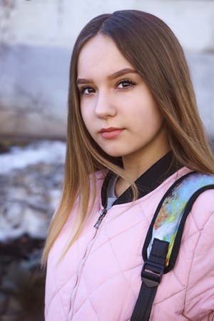 A girl in a pink jacket with a backpack is standing on the street