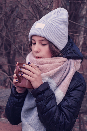 The girl holds a brown mug in her hands and blows on itの写真素材