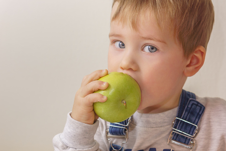A boy with gray eyes bites a green appleの写真素材