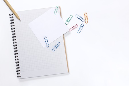 Notepad with a white sheet of paper with a pen and paper clips on white backgroundの写真素材