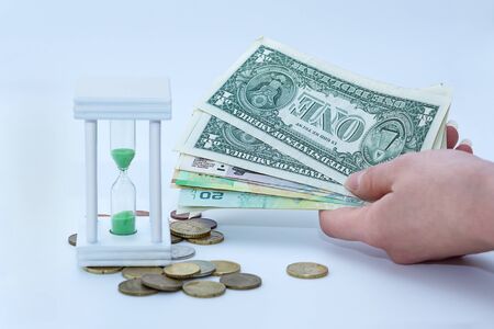 Female hand holds banknotes of different countries, next to an hourglass and coins of different countriesの写真素材