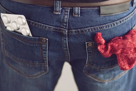 Pills and red panties in the back pockets of men's jeansの写真素材