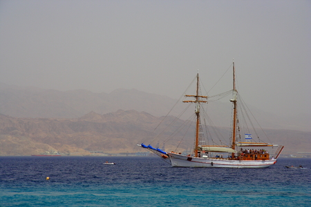Walking on a wooden boat in the Red sea, Israel, with their sails, and mountains in the background
