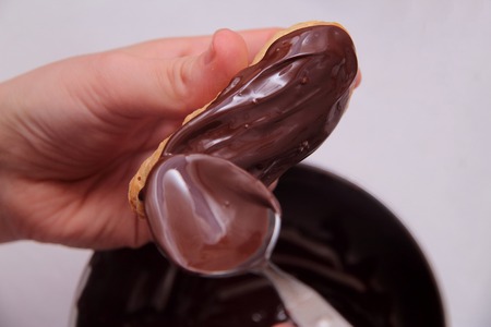 Eclairs or profiterole with chocolate and whipped cream. Spreading chocolate on top of eclair with spoon. Pastry Eclair imposes on a layer of melted chocolate with a spoonの写真素材