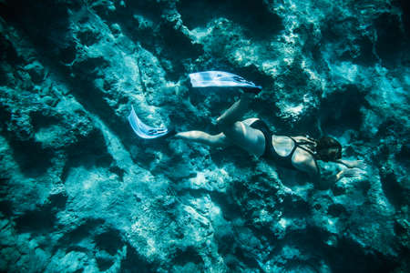 Underwater shooting girl dives underwater freediving in a black swimsuit in clear waterの写真素材