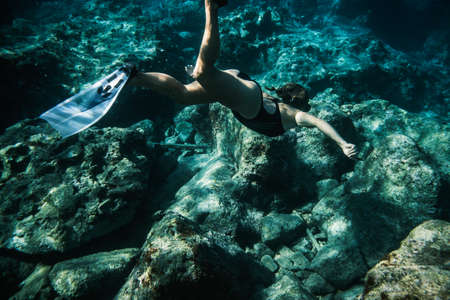 Underwater shooting girl dives underwater freediving in a black swimsuit in clear waterの写真素材
