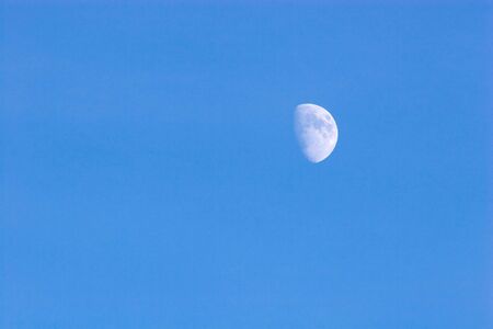 The white moon in the afternoon against the pure blue sky.