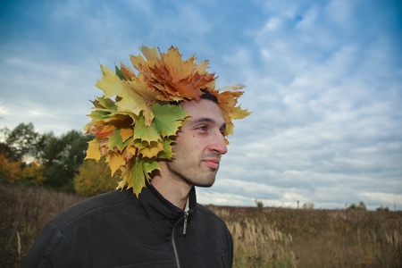 The young man with a wreath on a head, twisted from yellow leaves of a maple.の写真素材