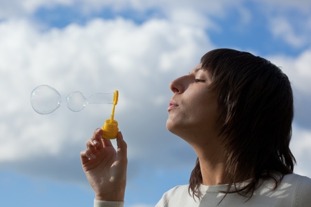 The girl starts up soap bubbles against the sky with clouds.
