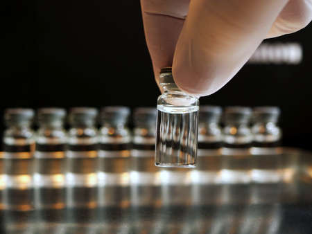 Filled vial held by fingers in a gloveの写真素材