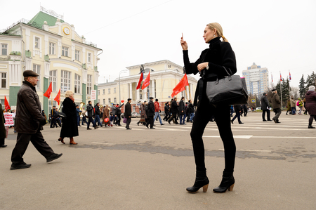 Orel, Russia, November 7, 2017: October Revolution anniversary meeting. Slender young woman taking photo of demonstrators with red flags backgroundのeditorial素材
