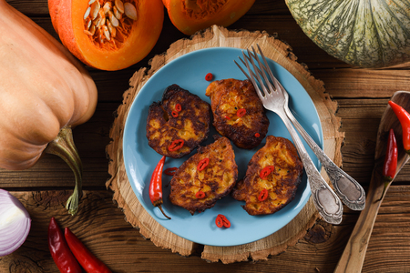 Pumpkin pancakes on wood slab decorated with chili peppers and raw pumpkins on rustic wooden background overhead viewの写真素材