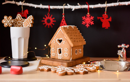 Small homemade gingerbread house, cookies and red Christmas toys on black background in toy kitchen...
