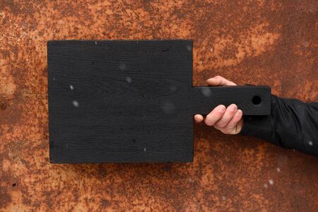 Black cutting board held in hand on corroded wood textured background copyspace horizontal