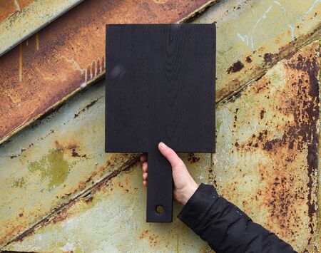 Black cutting board held in hand on corroded metal textured background copyspaceの写真素材