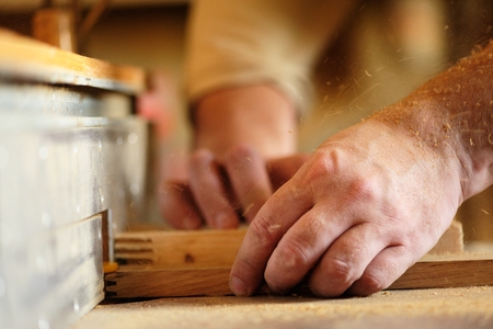 Carpenter's hands cutting piece of wood by cutter closeup