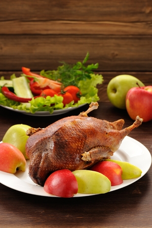 Roasted duck served with fresh vegetables and apples on wooden table verticalの写真素材