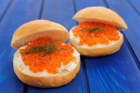 Delicious red caviar and green dill burgers on buns with cream cheese on deep blue table closeupの写真素材