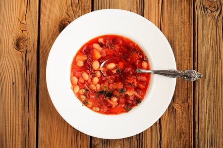 Portion of homemade Russian red beet soup borsch with bean, cabbage, potato with clean spoon on old wood table top view horizontalの写真素材