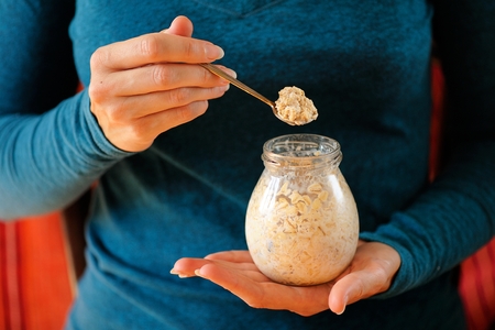 Woman's slender hands holding glass jar and spoon with overnight oats selective focus horizontalの写真素材