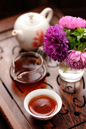 Small bouquet of purple and pink asters and black tea in chinese tradition on carved tea tray verticalの写真素材