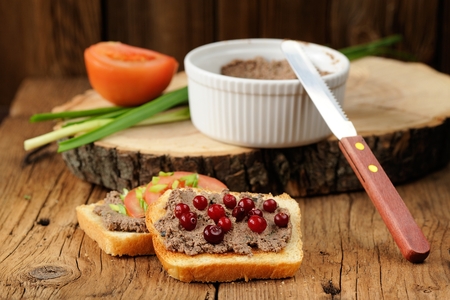 Homemade liver pate on toasts with tomatoes, scallion and cranberries on wooden board closeupの写真素材