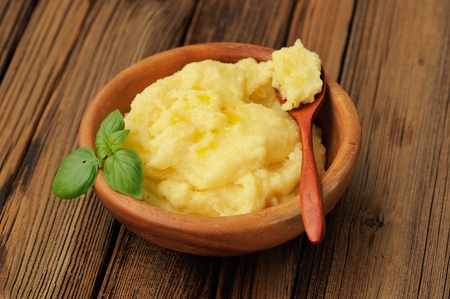 Polenta with green basil in wooden bowl with wooden spoon horizontalの写真素材