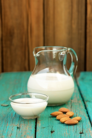 Homemade fresh almond milk in glass jar and glass bowl and whole almonds on shabby turquoise wooden table vertical copyspaceの写真素材