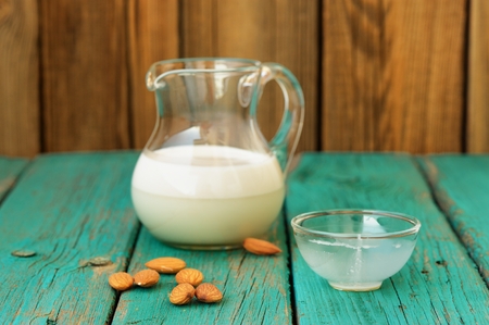 Homemade fresh almond milk in glass jar with empty glass bowl and whole almonds on shabby turquoise wooden table horizontalの写真素材