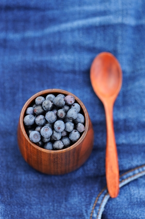 Fresh wild blueberries in wooden vase with wooden spoon on frayed indigo jeans selective focus  verticalの写真素材