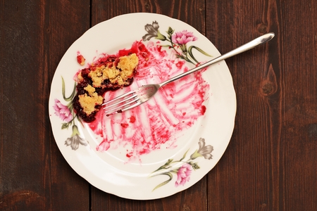 Remains of delicious cherry pie in white plate with long fork on wooden table top viewの写真素材