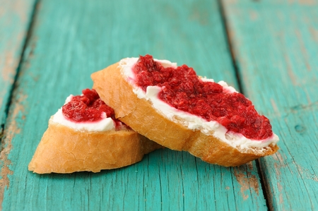 Two toasts with white cream cheese and homemade raspberry jam on old turquoise table closeupの写真素材