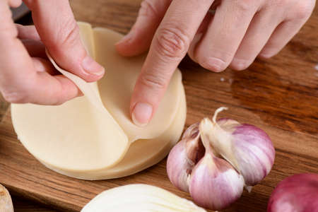 Cooking techniques. Closeup of woman hands making dumplings on wooden board closeup