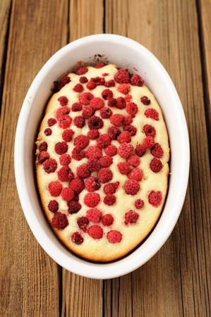 Homemade freshly baked sponge cake with wild raspberries in white oval baking pan on old rustic table verticalの写真素材